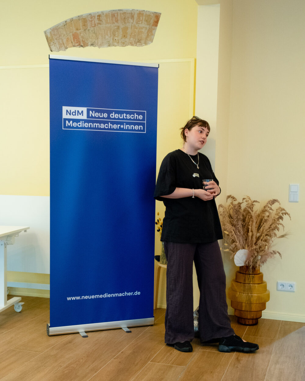 Redaktionelle Begleiterinn stellt sich vor dem NdM Roll-Up vor.