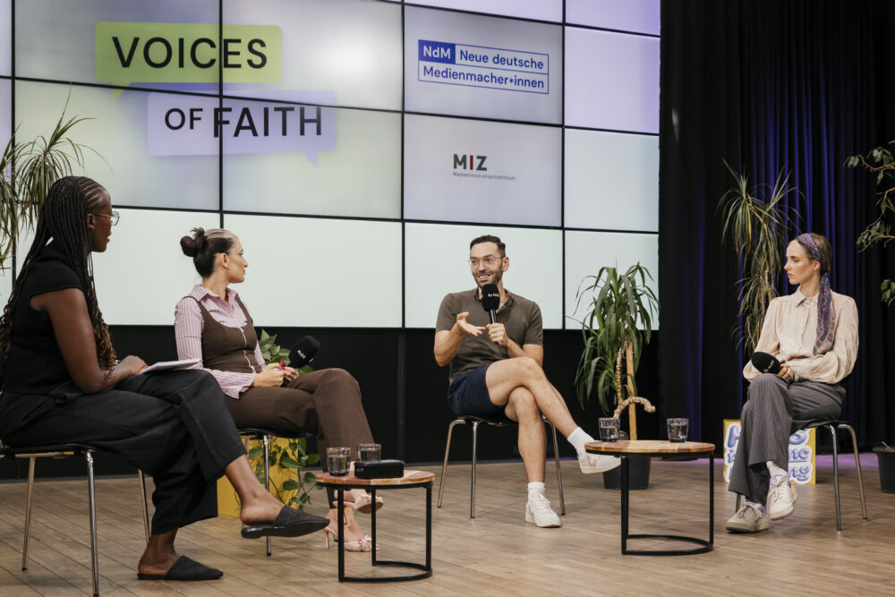 Ein Panel mit 4 Personen sitzt im Studio von ALEX. Im Hintergrund ist eine Leinwand mit Logos und der Schrift "Voices of Faith".