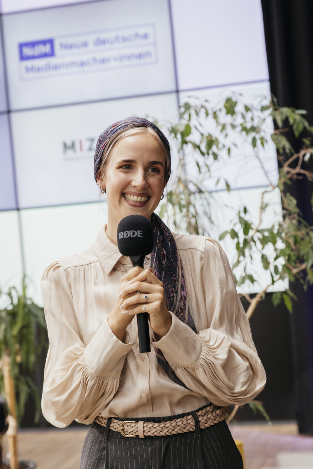 Die Speakerin Leni Braun spricht in ein Mikrofon. Dahinter ist das Logo von NdM eingeblendet.