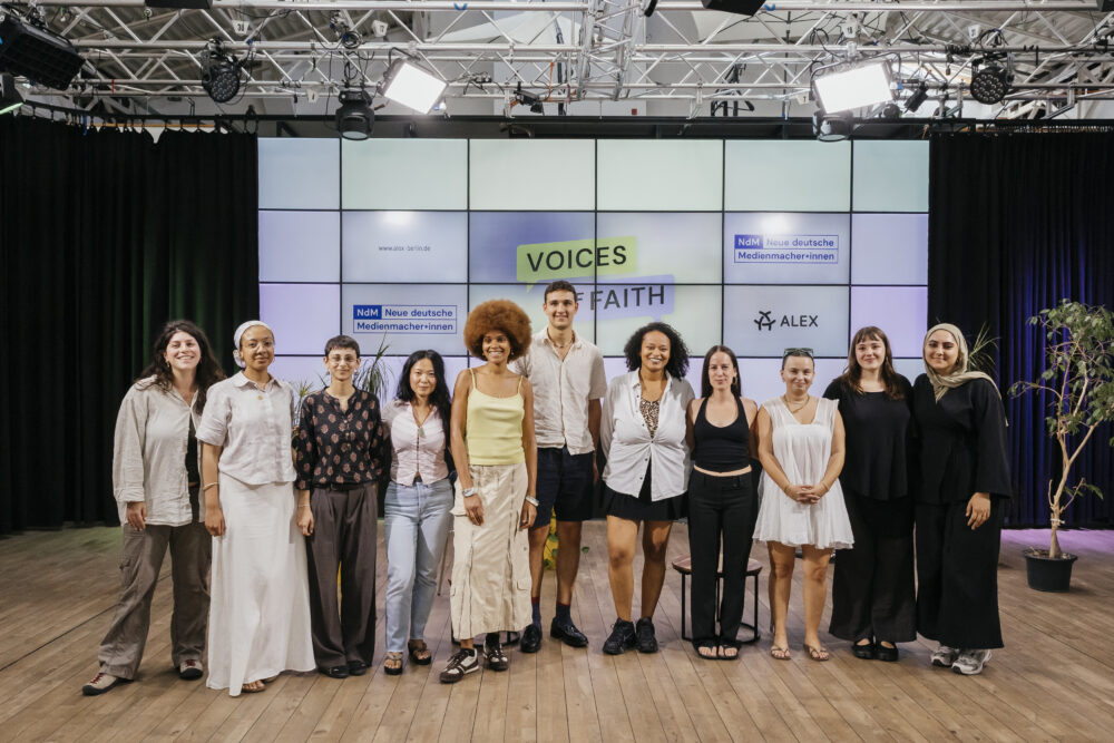 Gruppenfoto von 11 Personen in einer Reihe im Studio von ALEX. Im Hintergrund ist das Set für die Sendung "Voices of Faith".