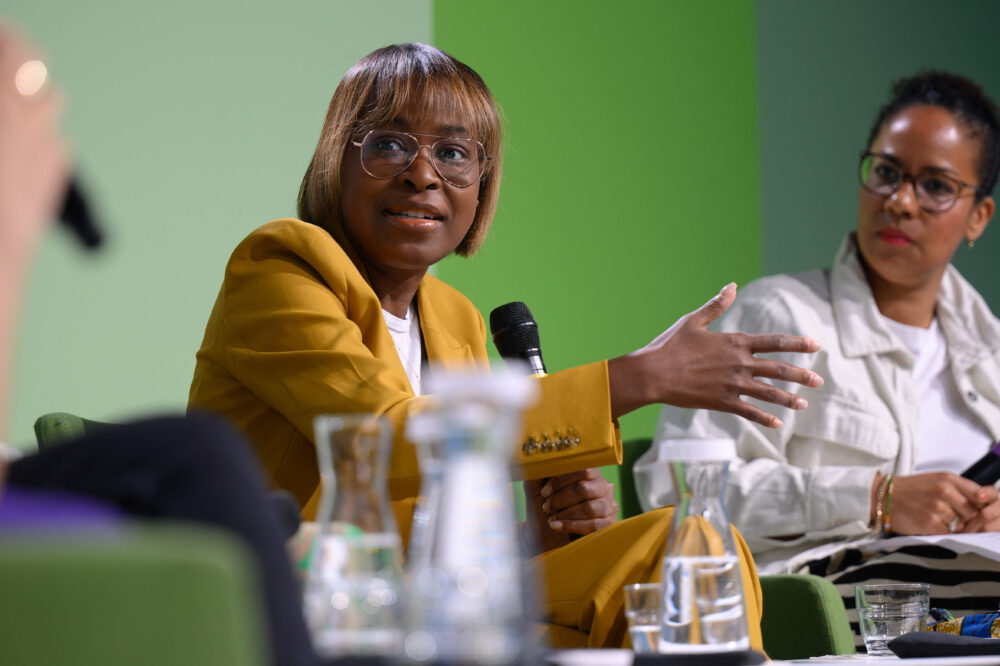 Das Bild zeigt eine Paneldiskussion zum Thema: "Democratic Reporting in Times of Elections. Wie wird der Politikjournalismus seiner demokratischen Verantwortung gerecht?" in 2024. Zwei Frauen sitzen auf der Bühne. Eine der beiden erklärt etwas.