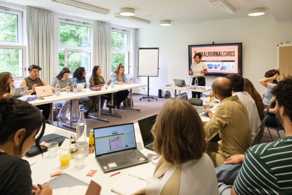 Lokaljournalismus-Workshop, vorne steht Janina Preuß (Halterner Zeitung), im Raum
sitzen Mentees an ihren Tischen, hören zu und schreiben Notizen