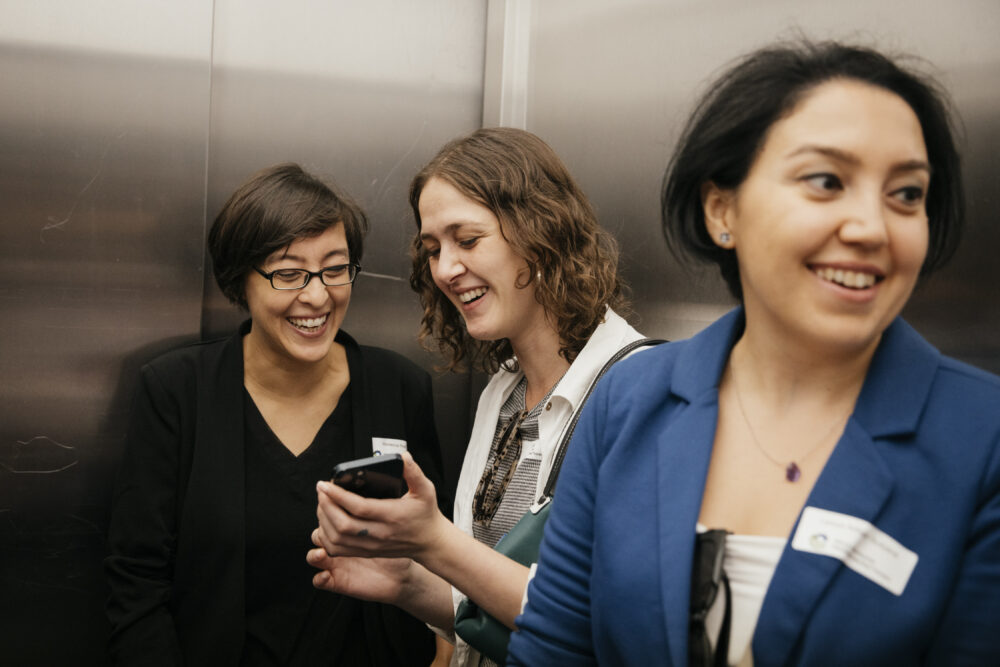 Das Bild zeigt drei lachende Personen bei einer Veranstaltung des Mentoringprogramms im Fahrstuhl.