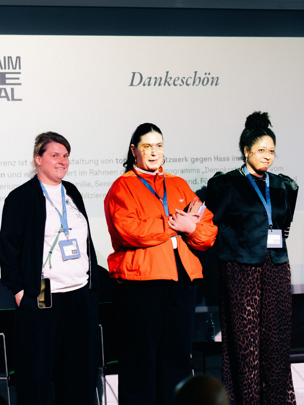 Drei Personen mit Namensschildern stehen nebeneinander vor einer Wand mit dem Schriftzug 'Dankeschön'