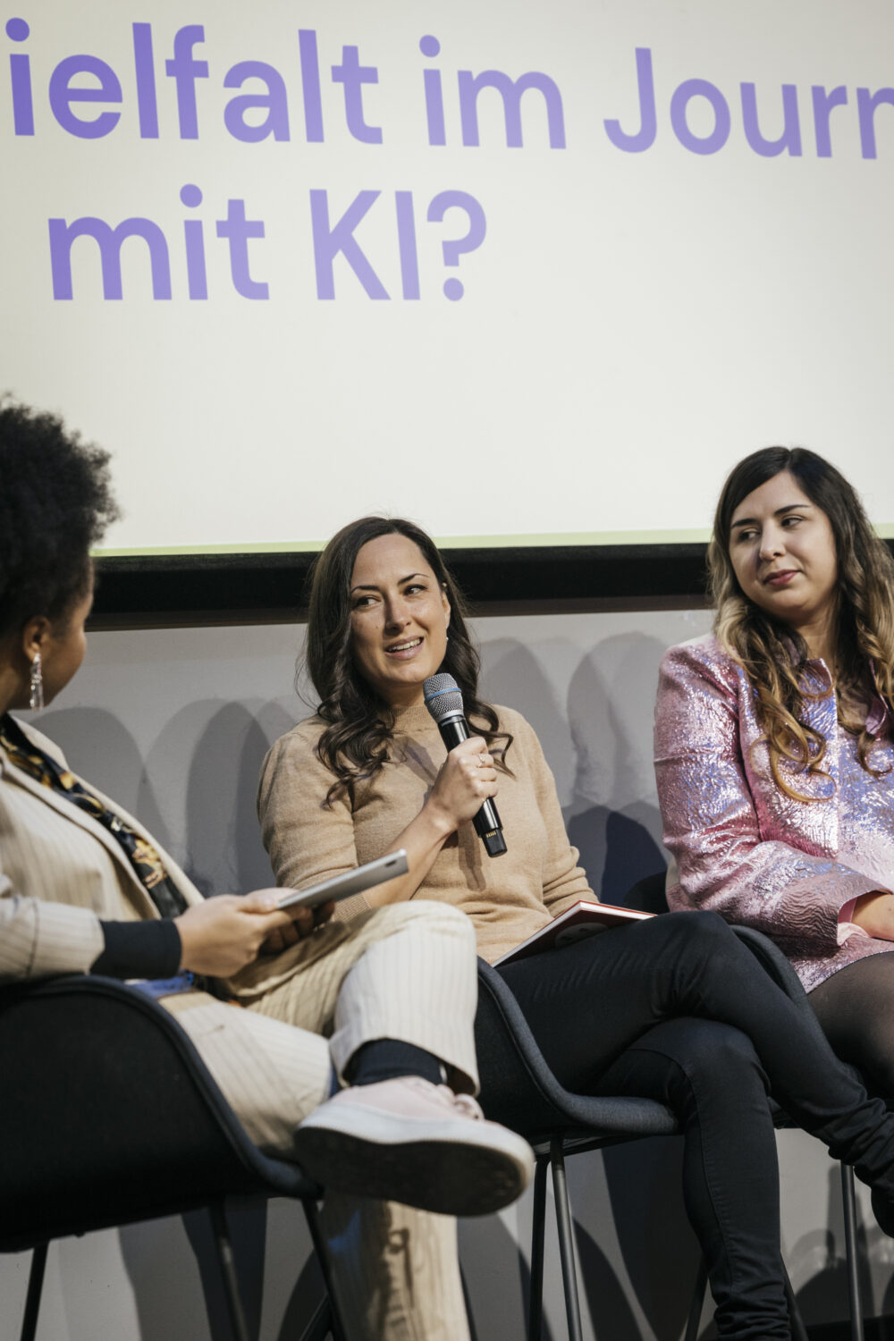 Drei Frauen sitzen auf einem Panel, die Person in der Mitte spricht ins Mikrofon.