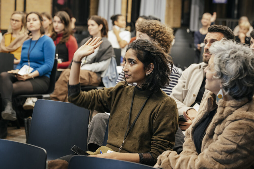 Das Bild zeigt Teilnehmer*innen auf einer Veranstaltung. Eine Person meldet sich.